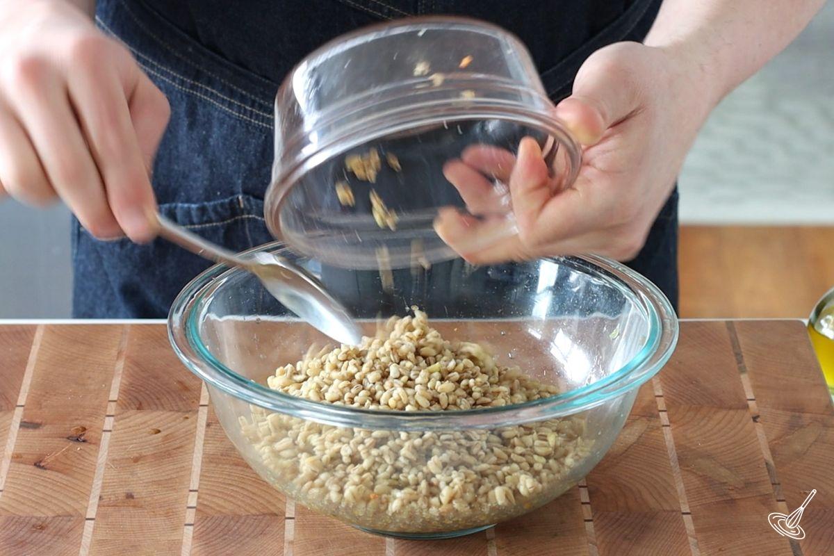 Someone adding cooked barley to a large bowl. 
