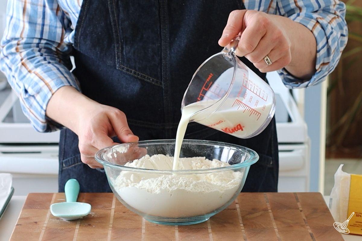 Someone pouring in buttermilk into a large bowl of dry ingredients.