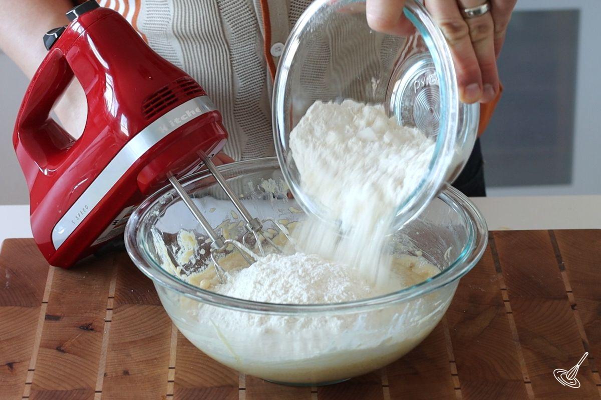 Someone adding flour to a bowl of cake batter.