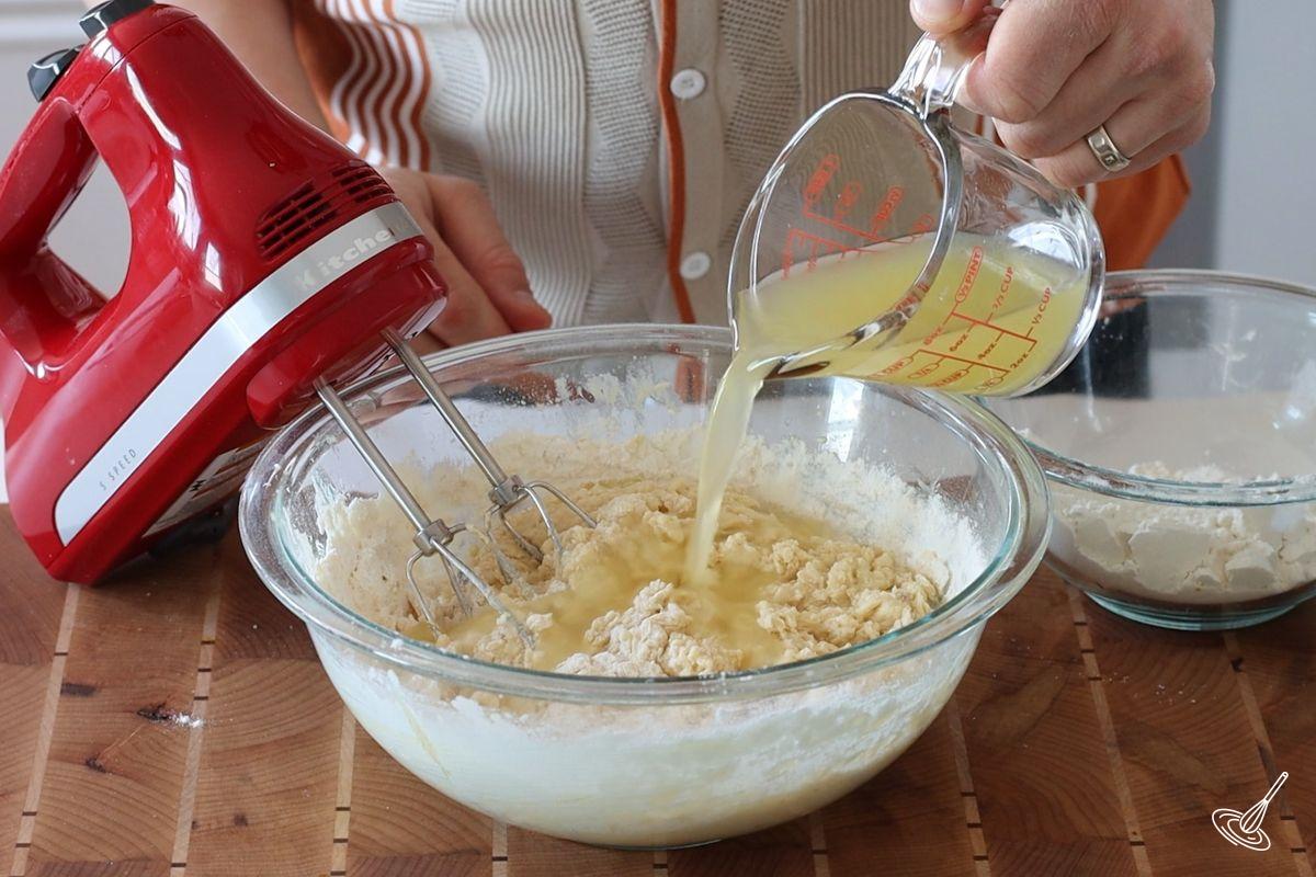 Someone pouring pineapple juice in a bowl of cake batter.