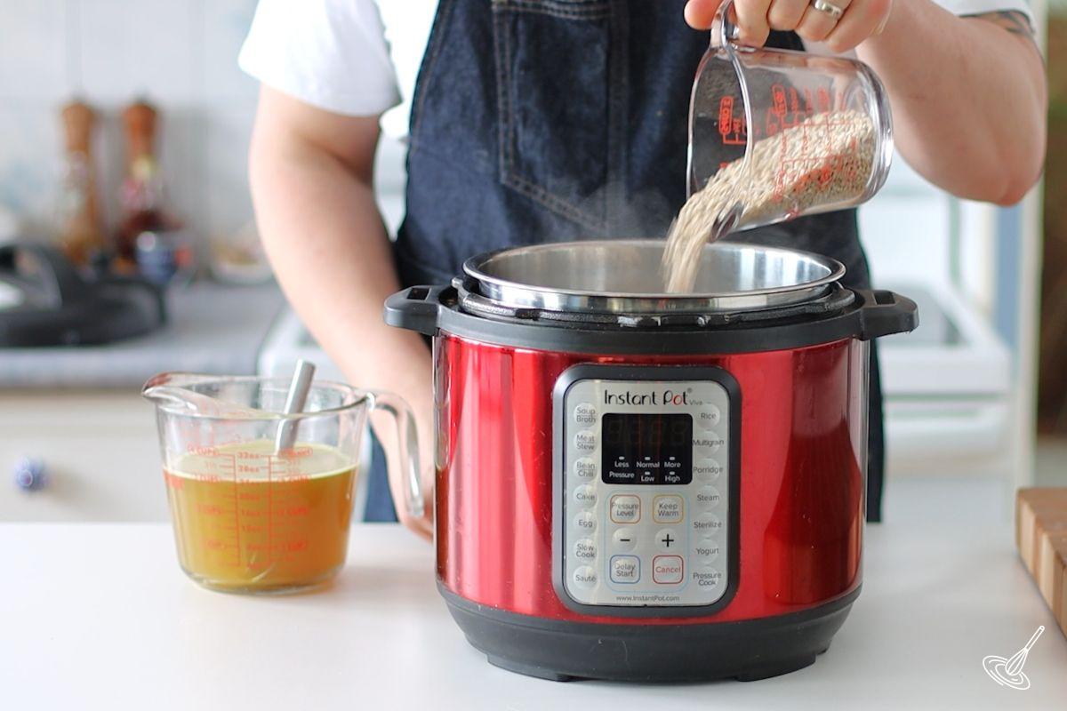 Someone adding barley to the bowl of a pressure cooker.