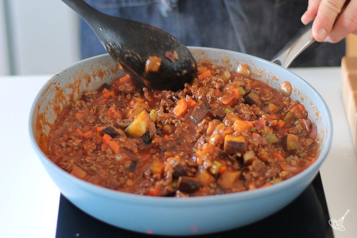 Someone stirring aubergine bolognaise in a large pan.