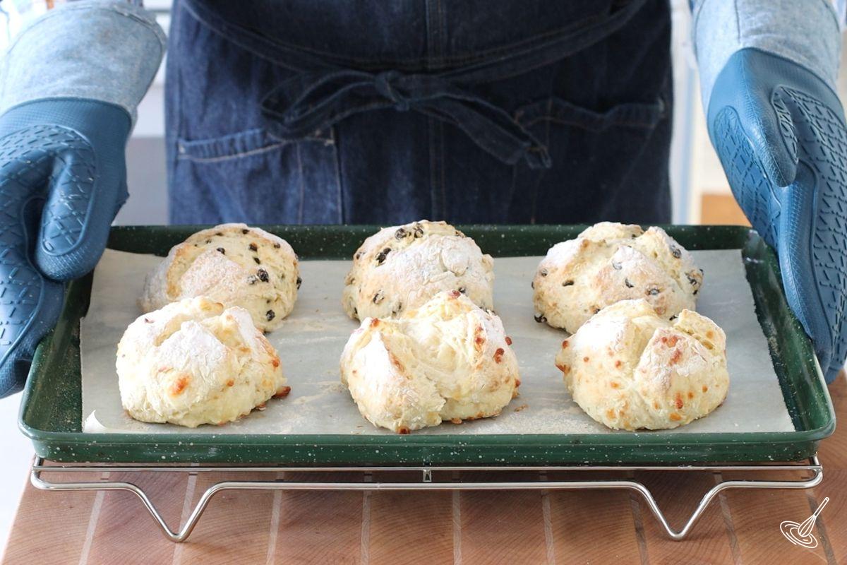 Someone placing a tray of baked Irish Soda bread rolls on a cooling rack. 
