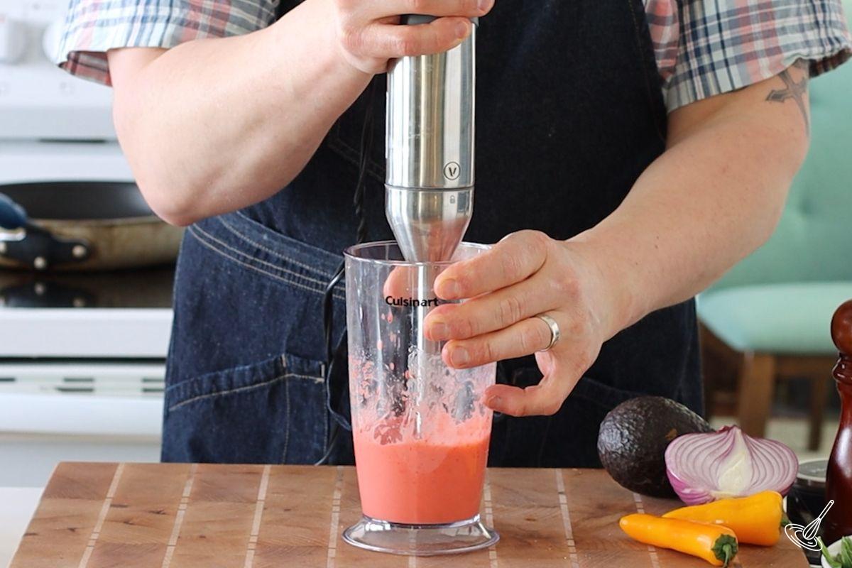 Someone using a stick blender to puree Strawberry salad dressing.