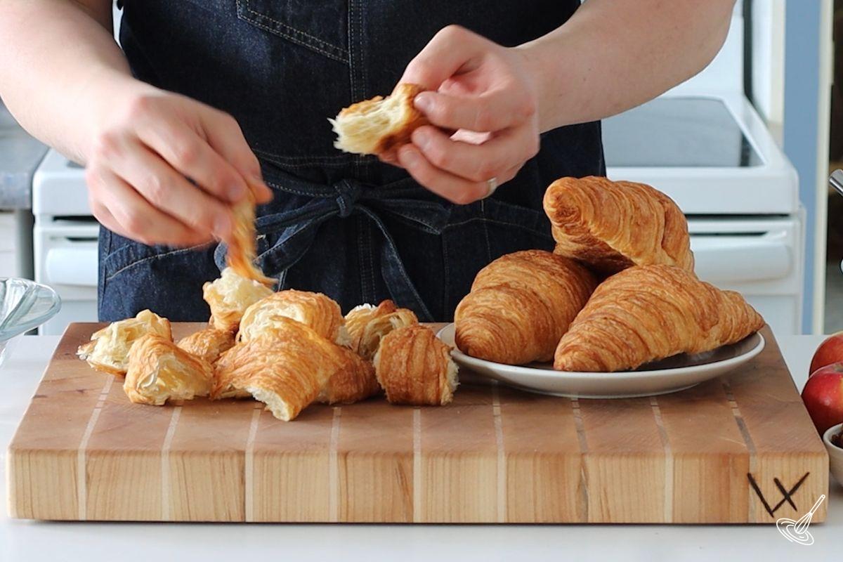 Someone tearing up croissants into pieces using their hands.