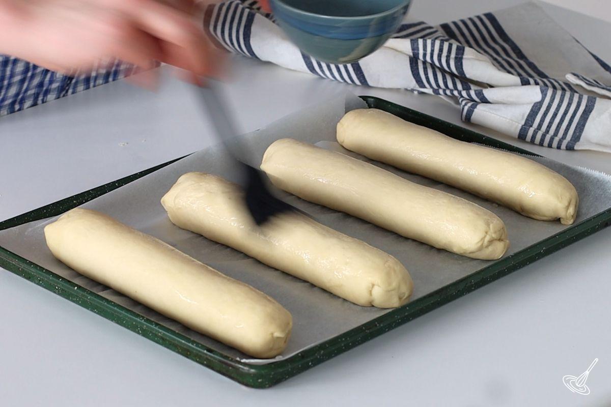 Someone brushing brioche sub roll with water. 
