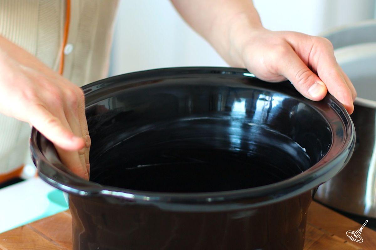 Someone coating a slow cooker crock with butter. 