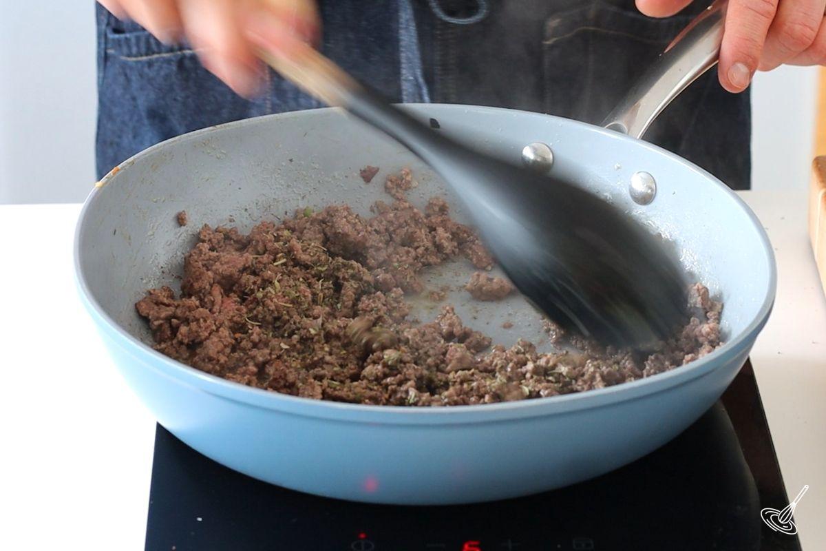 Someone cooking ground been in a large frying pan. 