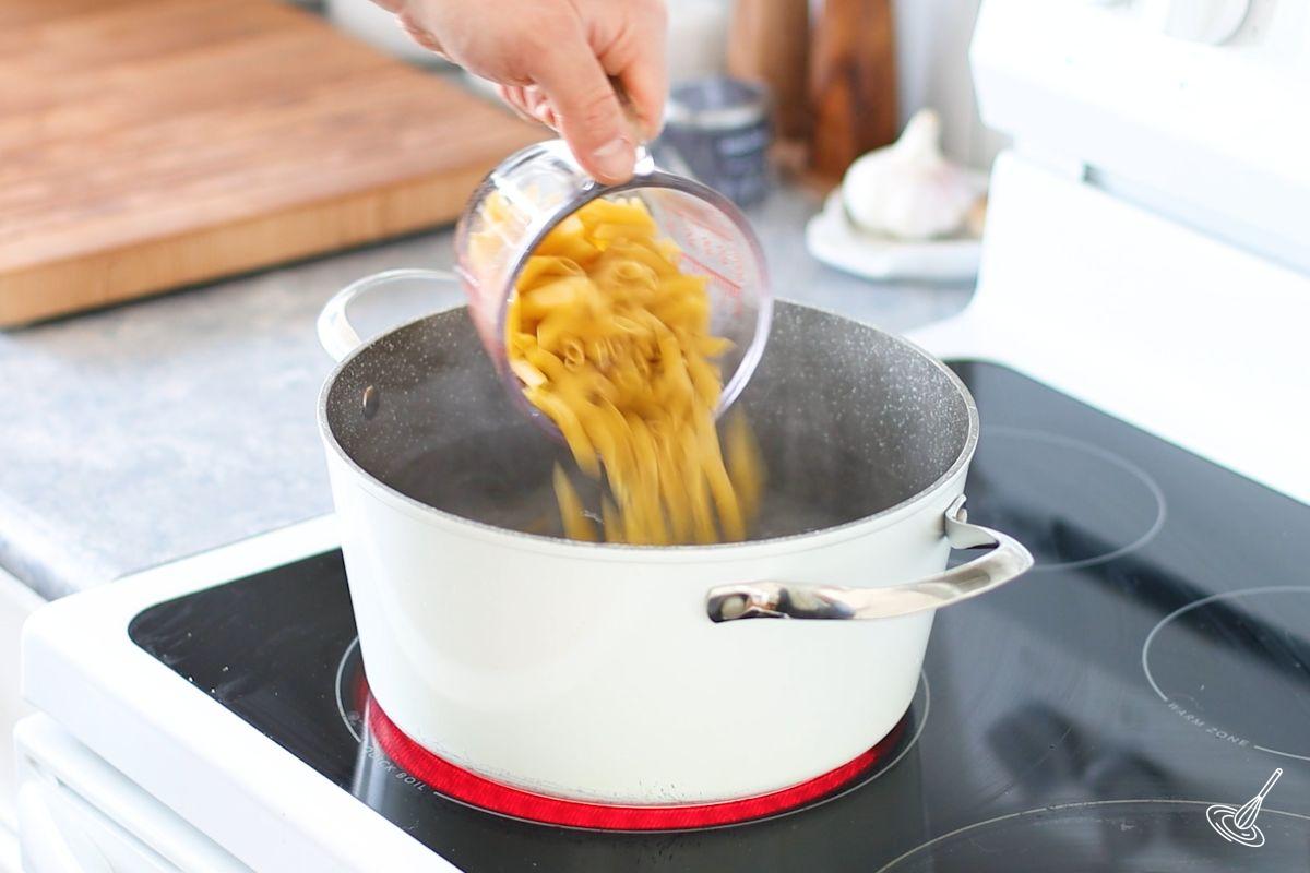 Someone adding penne pasta to a large pot of boiling water. 