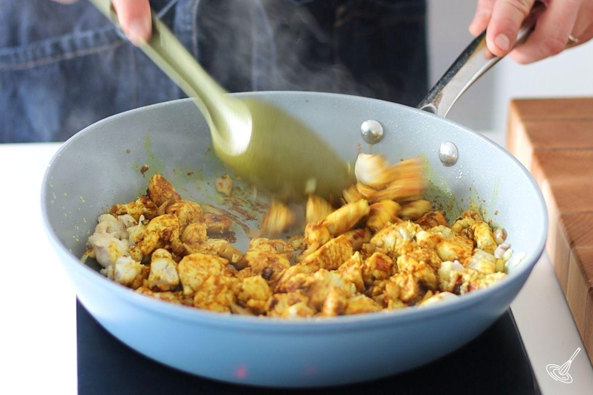 Someone stirring curry chicken in a large pan. 
