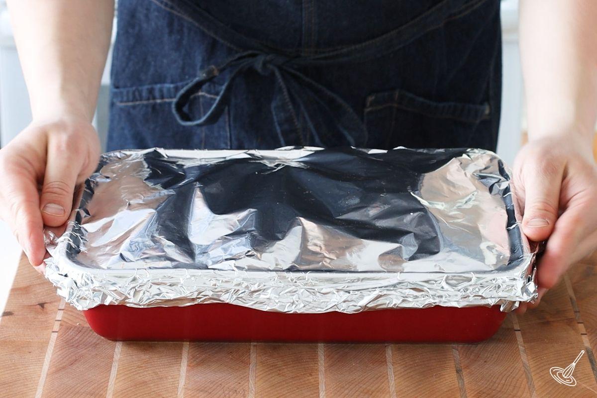 Someone putting foil on top of a baking dish.