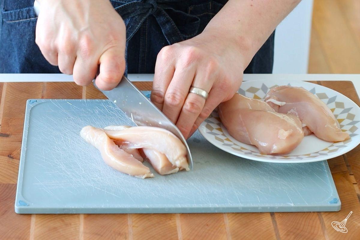 Someone cutting a chicken breast into cubes.