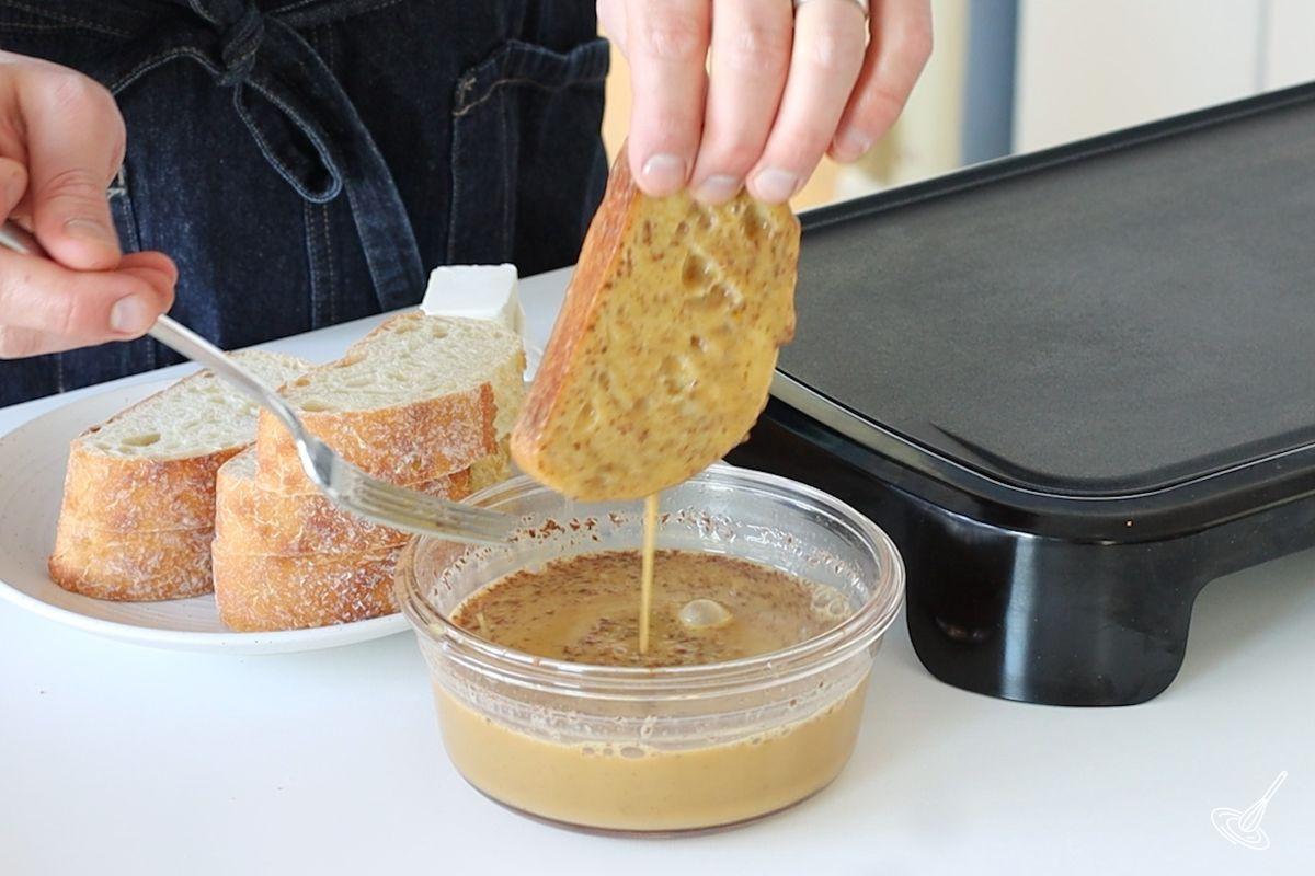 Someone dipping a thick slice of bread in a French toast egg mixture.