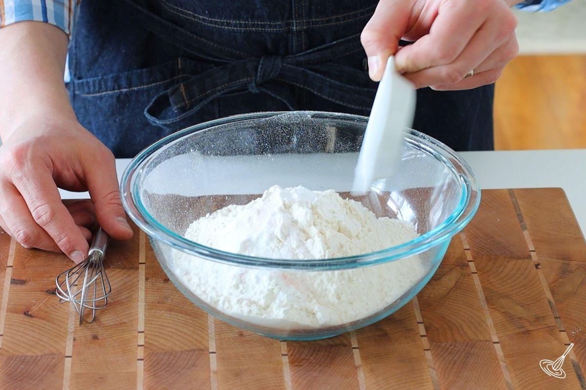 Someone adding salt to a large bowl of flour. 