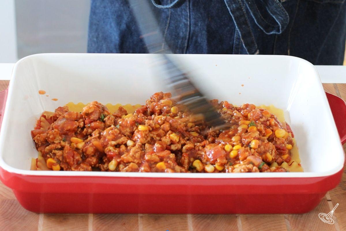 Someone spreading meat sauce on top of lasagna noodles.