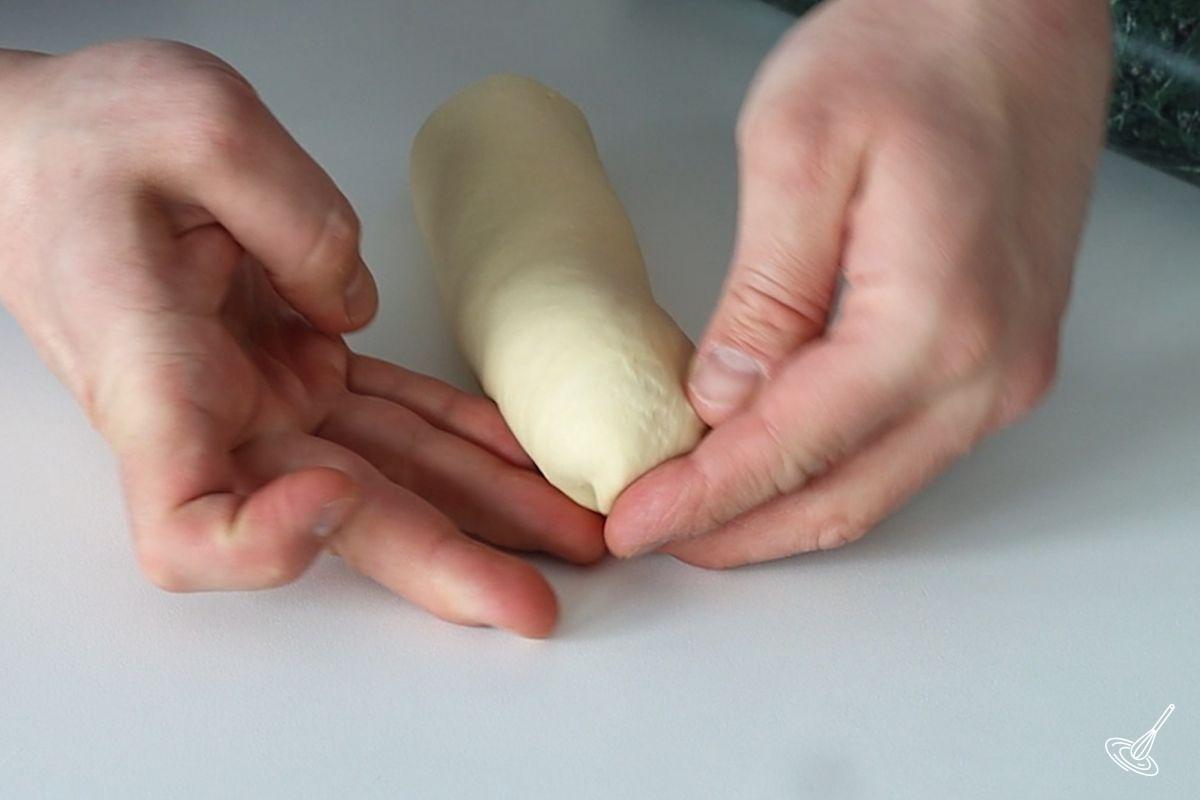 Someone using their fingers to tuck in the end of a brioche sub roll.