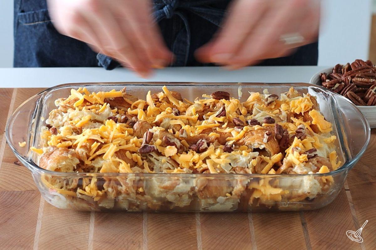Someone sprinkling pecans on top of a maple croissant bake before it goes in the oven.