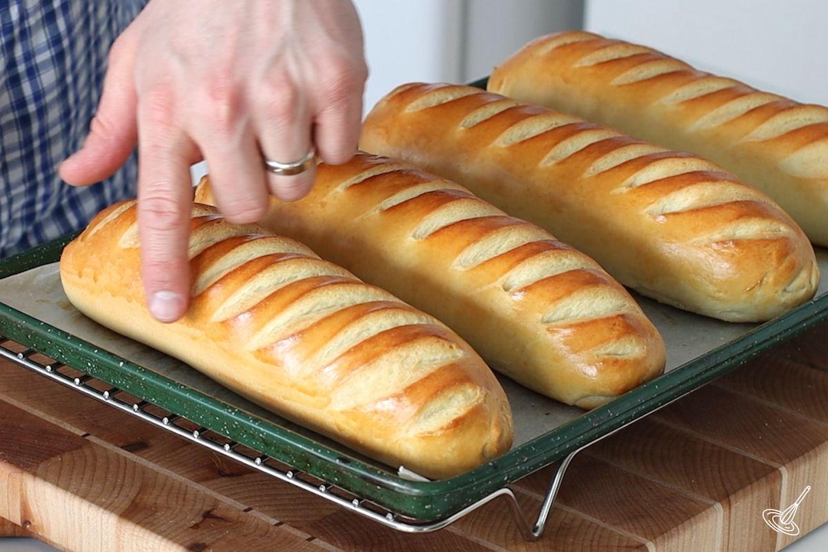 A tray of brioche sub rolls on a cooling rack.
