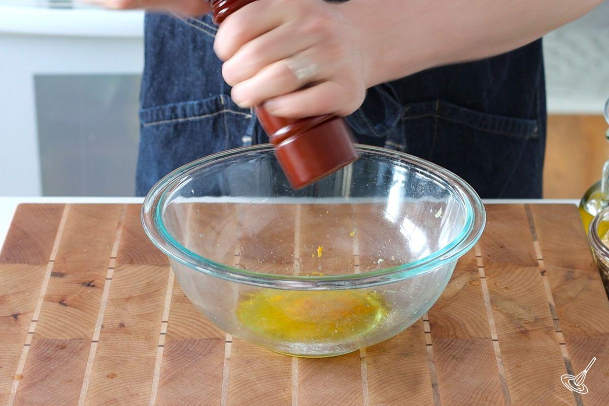Someone adding pepper to a large bowl containing olive oil. 