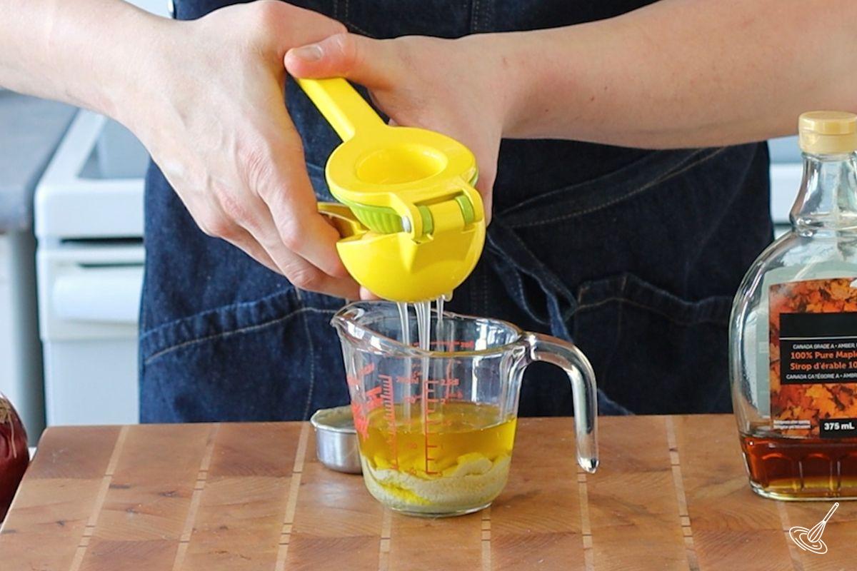 Someone squeezing lemon juice into a container of tahini dressing.