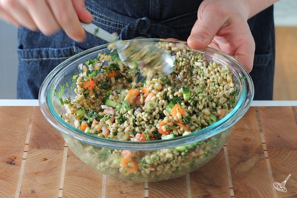 Someone stirring a large bowl of barley tabbouleh salad.