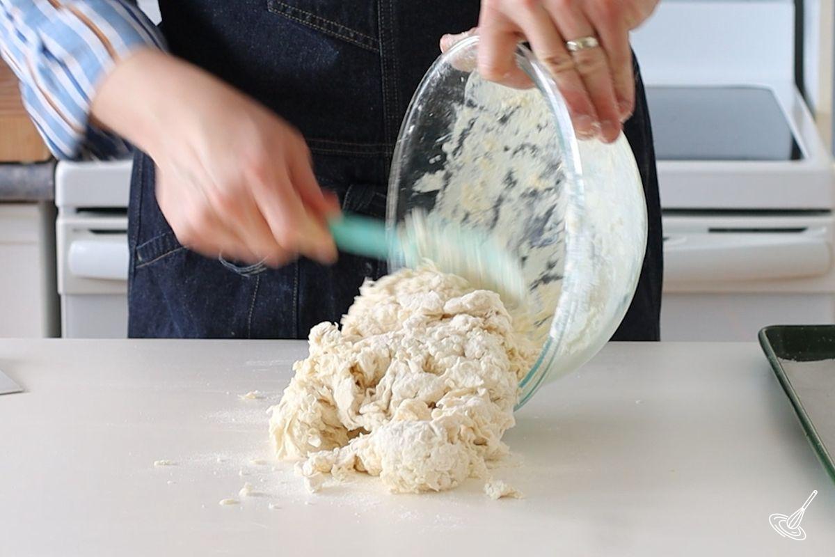 Someone pouring a bowl of irish soda bread rolls dough on the kitchen counter. 