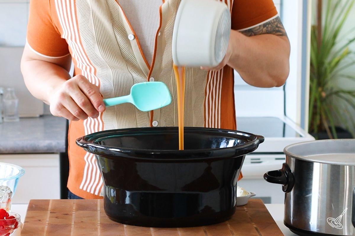 Someone pouring caramel in the crock of a slow cooker. 