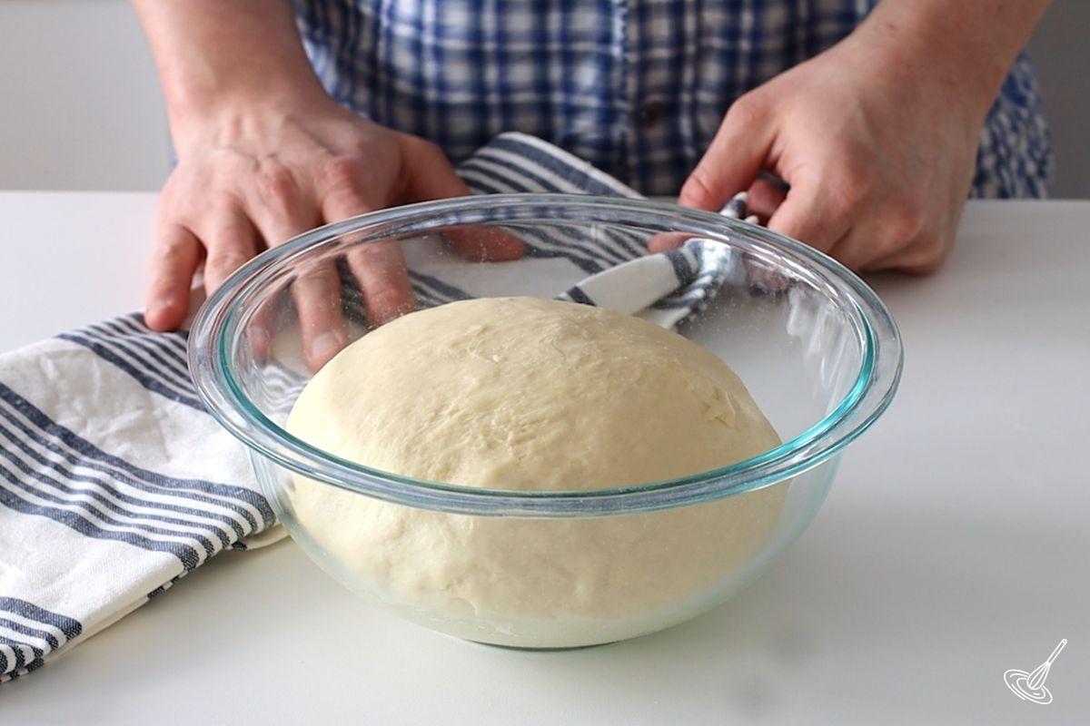 A ball of brioche bun roll dough rising in a large bowl.