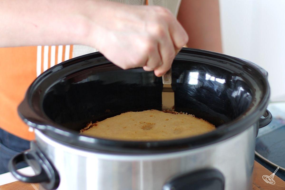 Someone using a spatula to loosen up the sides of the Crockpot Pineapple Upside Down Cake. 