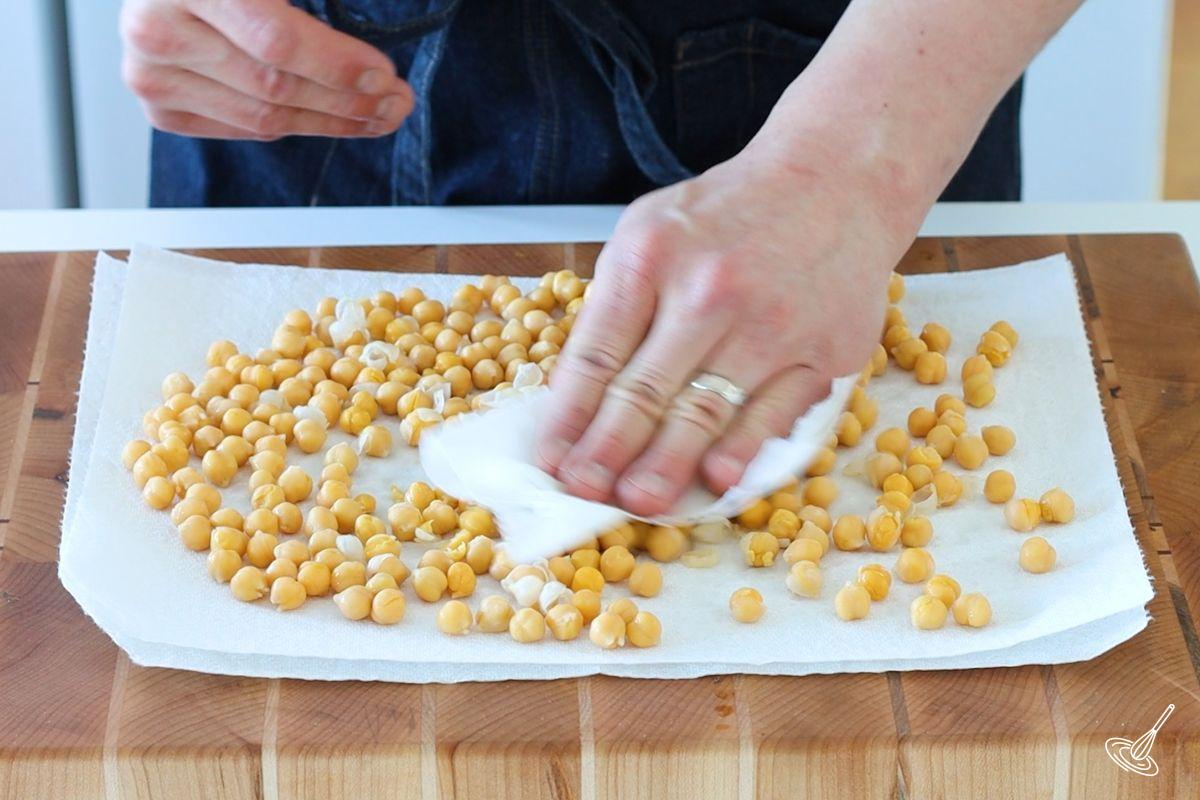 Someone using a paper towel to rub the skins off of chickpeas.