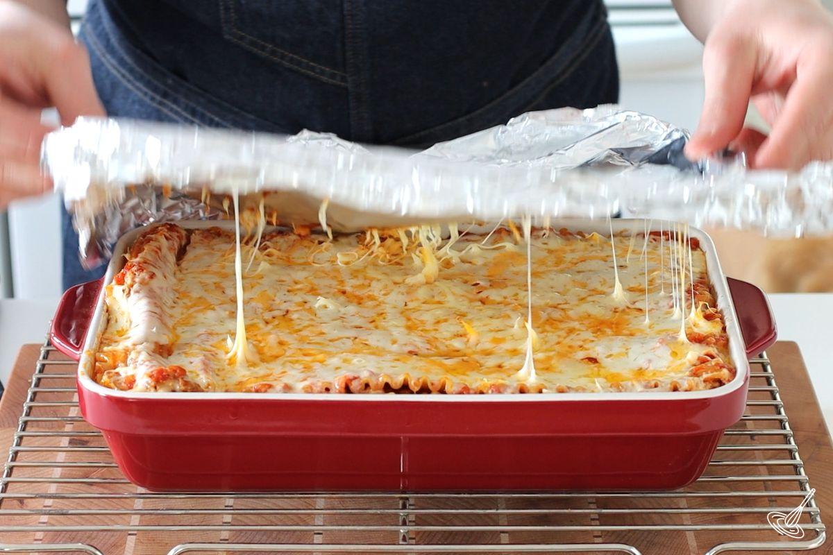 Someone removing foil cover from a baked Barbecue Turkey Lasagna.