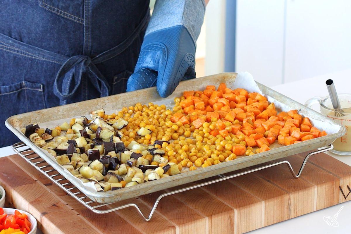 Someone taking a sheet pan of roasted vegetables out of the oven. 
