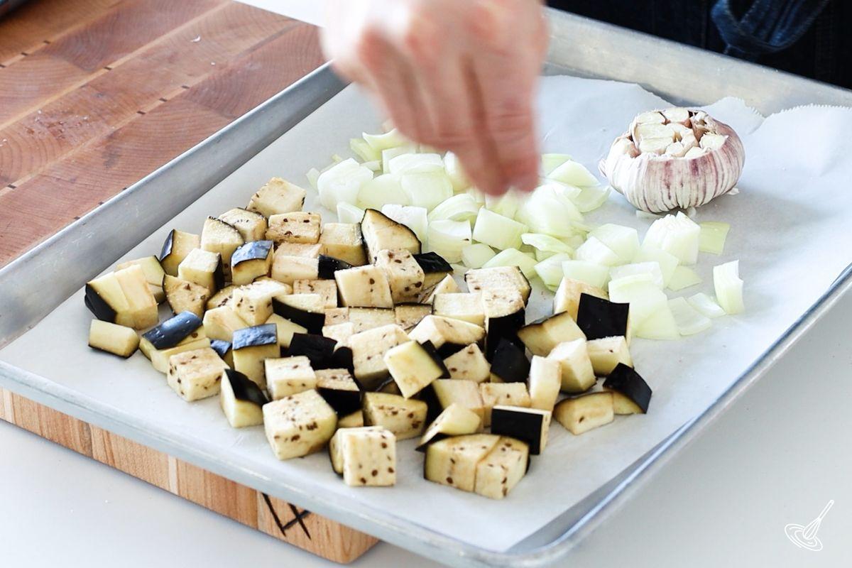 Someone sprinkling salt on a tray of chopped vegetables.