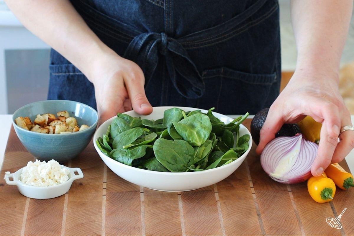 Someone placing a bowl of baby spinach on the counter.