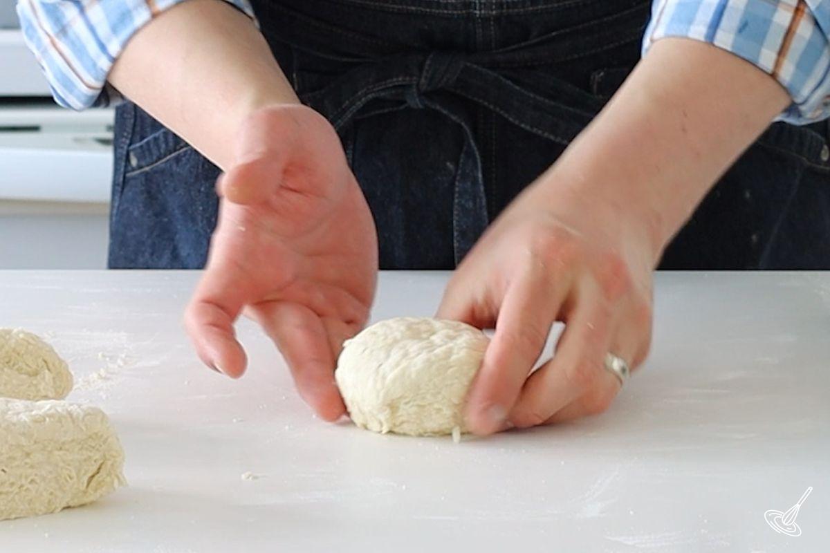Someone using their hands to shape an irish soda bread roll.