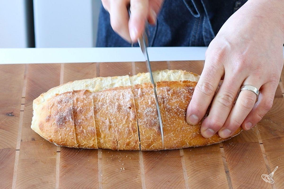 Someone cutting slices in a loaf of bread.