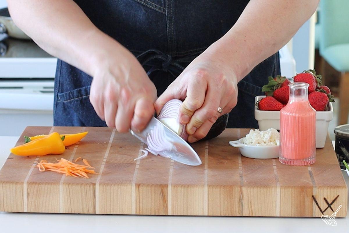 Someone using a large knife to slice an onion.