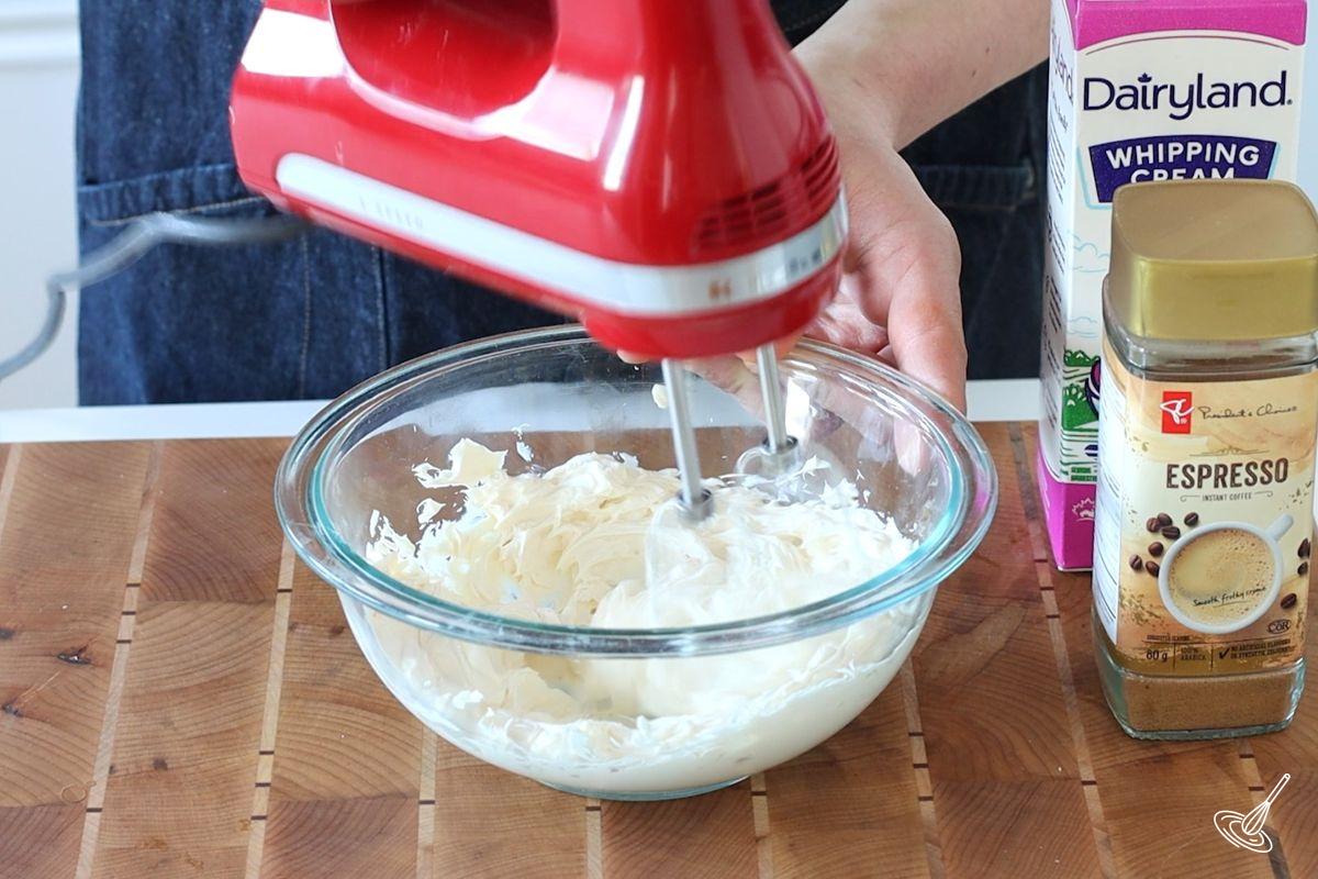 Someone using a hand blender to mix cream cheese in a bowl. 