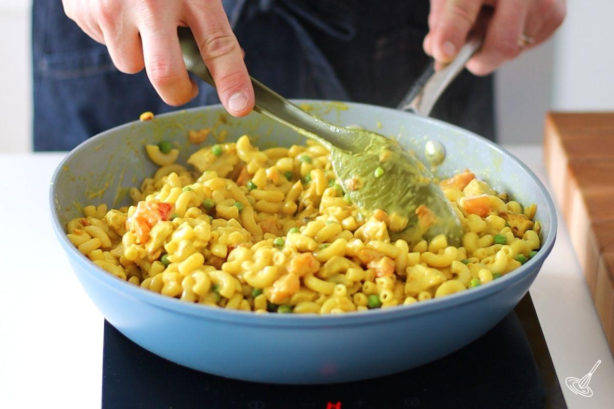 Someone stirring cooked chicken curry pasta in a large pan.