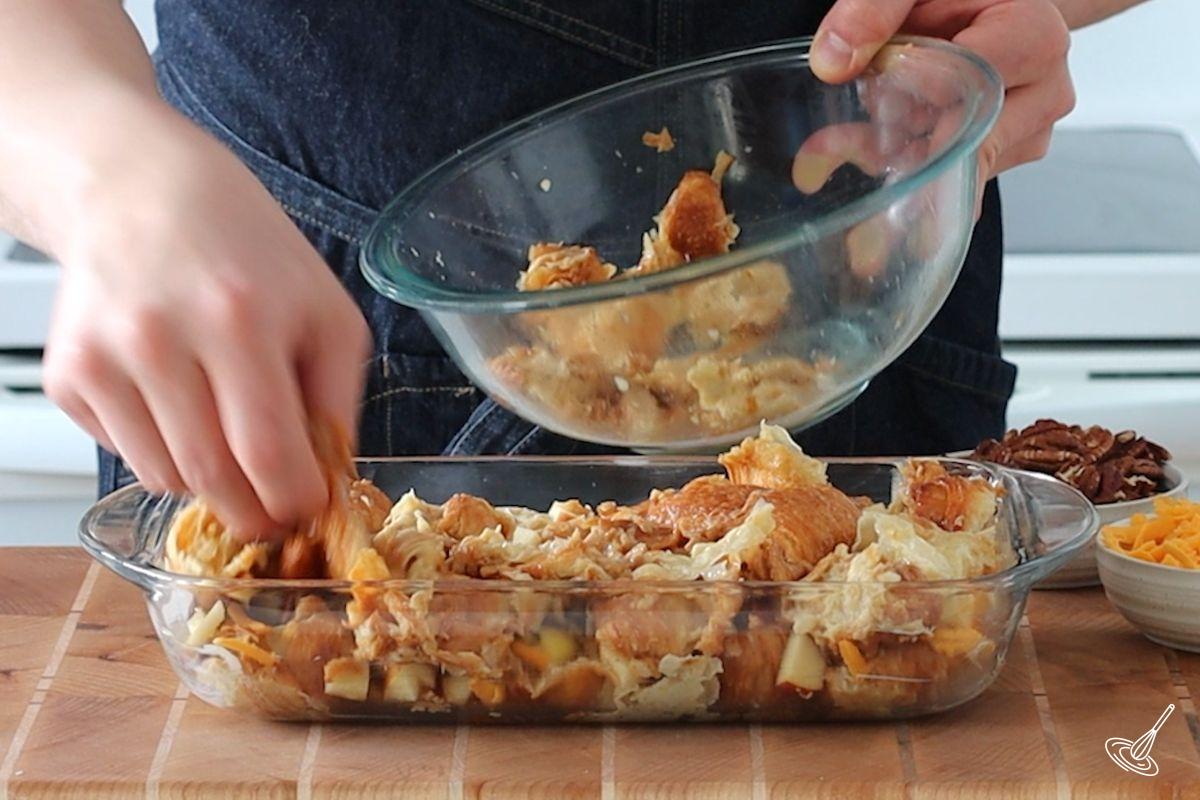 Someone placing pieces of custard-soaked croissant in a baking dish.