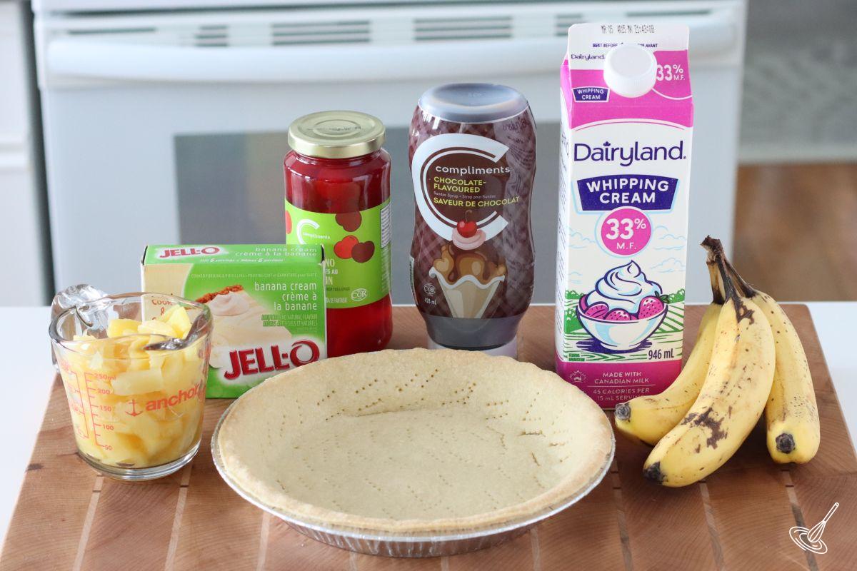 Recipes on the counter to make banana split including a baked pie shell, banana, and pineapple pieces.