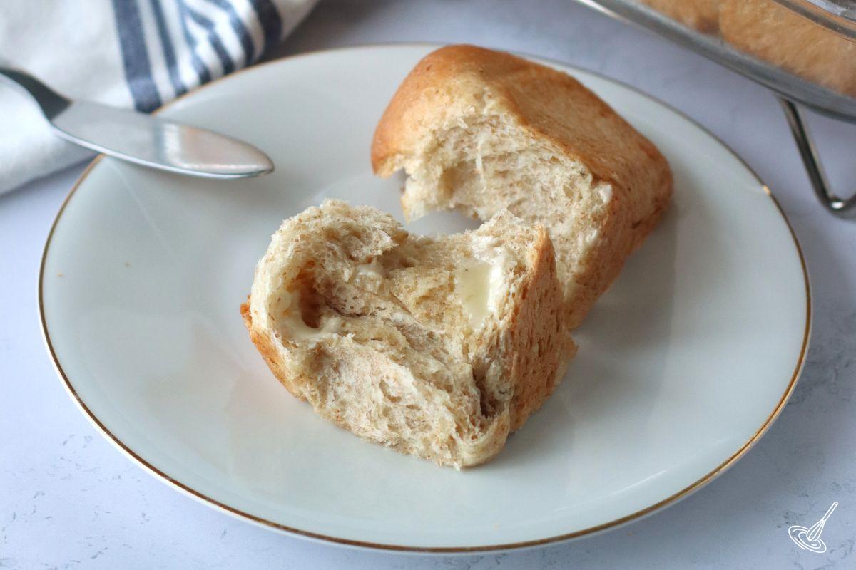 A buttered honey whole wheat dinner roll on a plate. 