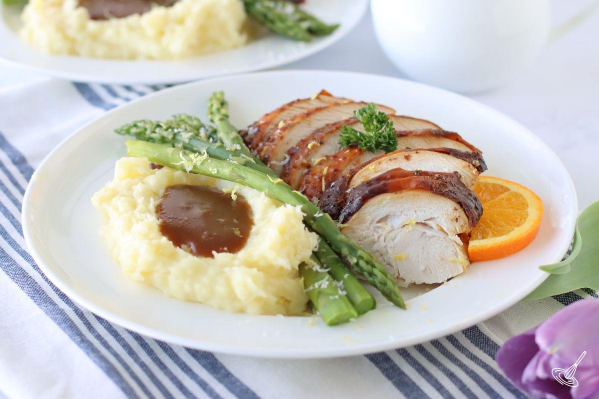 Maple Orange Turkey Roast slices on a plate with a side of mashed potatoes and asparagus.