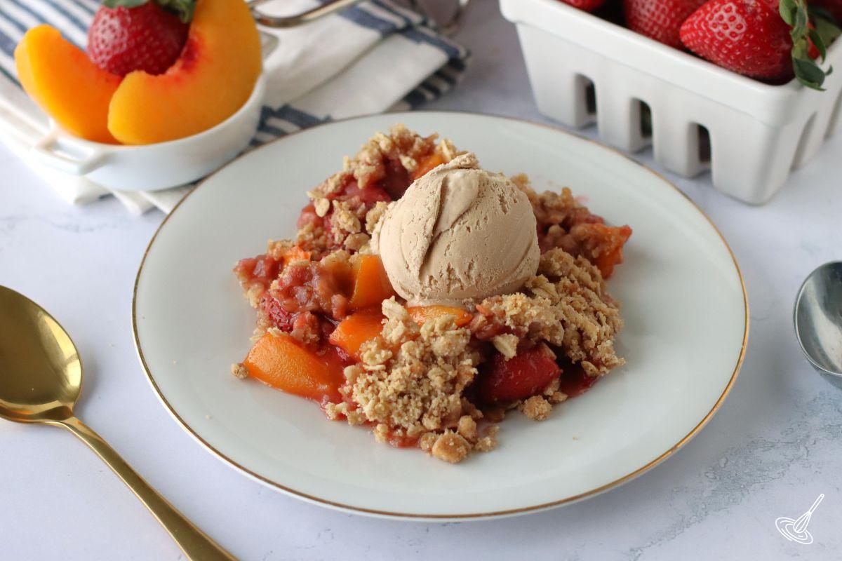 Strawberry Peach Crisp on a plate with a scoop of ice cream on top.