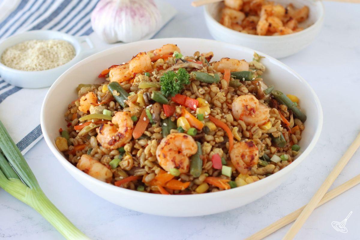 Barley fried rice in a serving bowl, garnished with pan-fried shrimp.