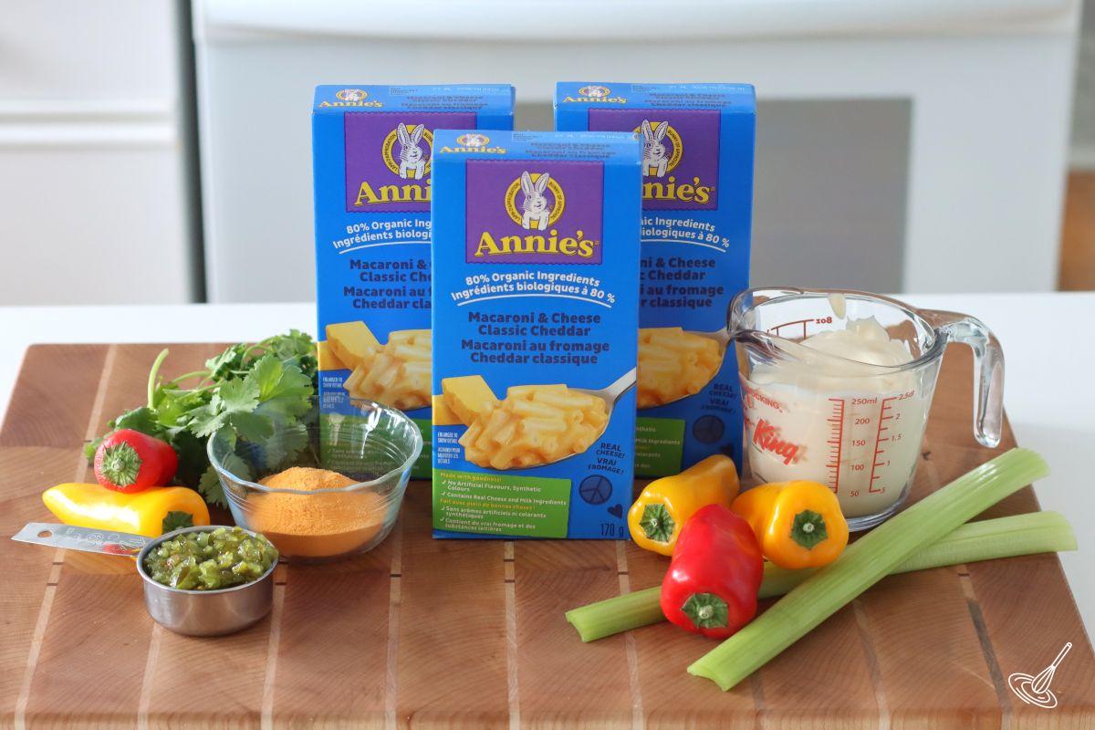 Ingredients on the kitchen counter to make Cheesy Macaroni Salad including mayonnaise, vegetables, and boxes of macaroni and cheese.