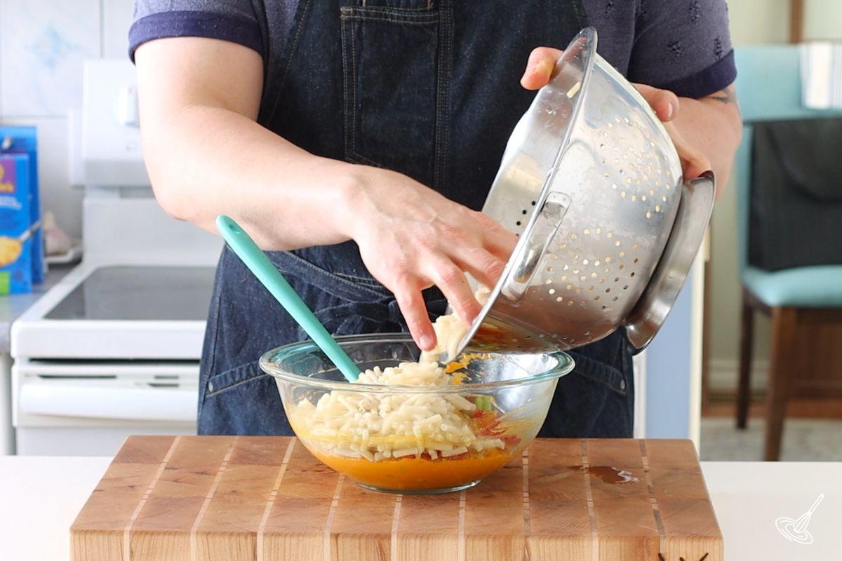 Someone adding cooked macaroni noodles to a bowl of cheesy dressing. 