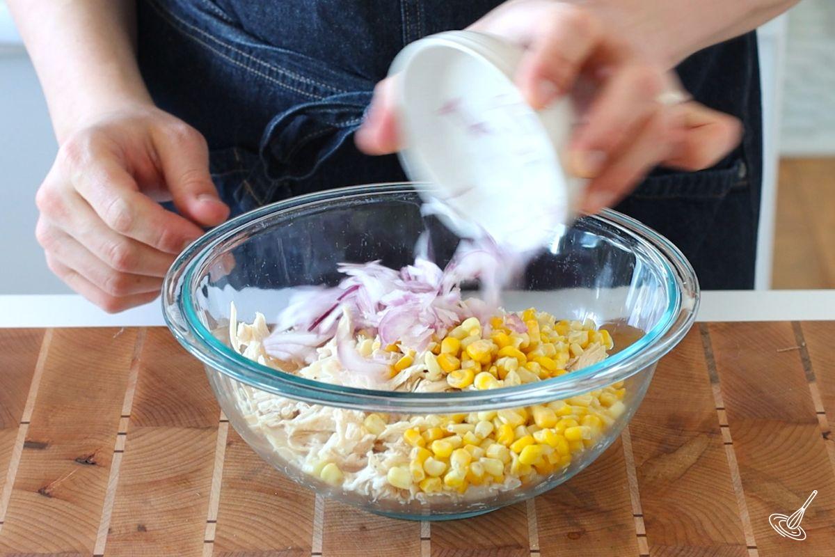 Someone adding chopped red onion to a large bowl of shredded turkey. 