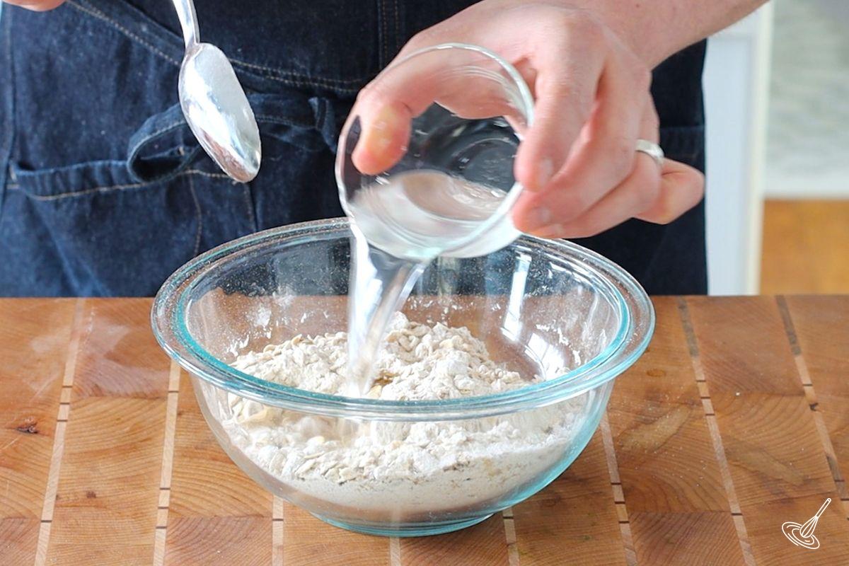 Someone adding melted coconut oil to a bowl of crumble ingredients.