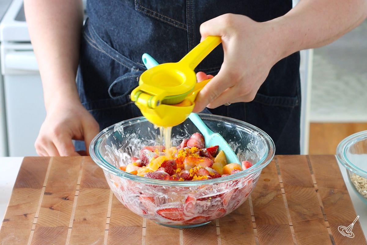 Quelqu'un qui presse du jus d'orange frais sur un bol de fraises et de pêches.